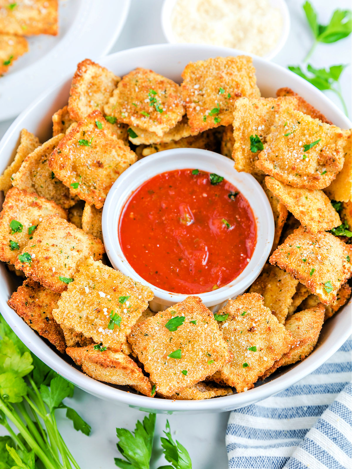 Marinara sauce in a small bowl surrounded by toasted ravioli.