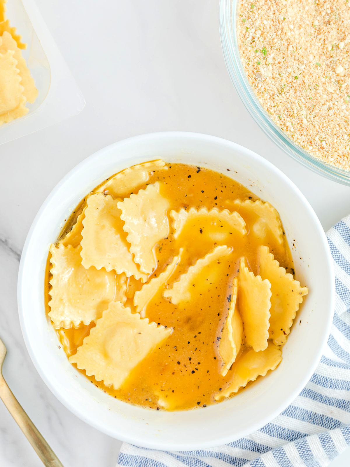 Ravioli being dipped in an egg mixture.