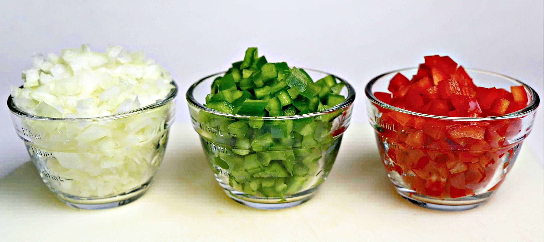 Bowls of diced onion, diced green bell peppers, and diced red bell peppers.