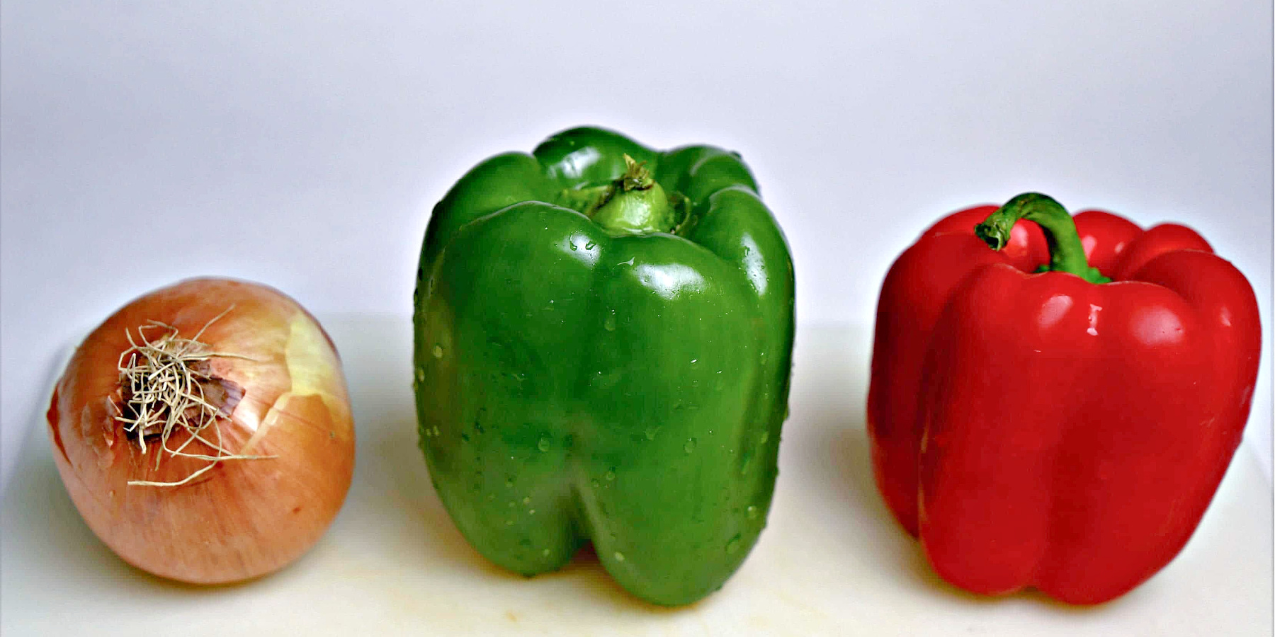 Yellow onion, green bell pepper, and red bell pepper on a cutting board.