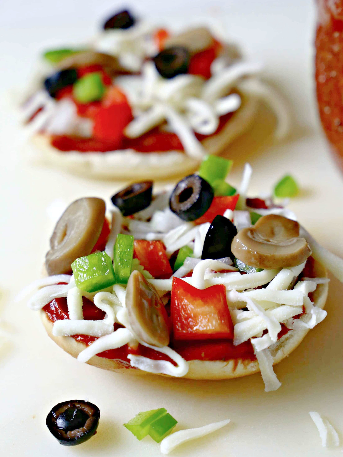 Two bagel halves topped with pizza sauce, mozzarella cheese, and veggies.