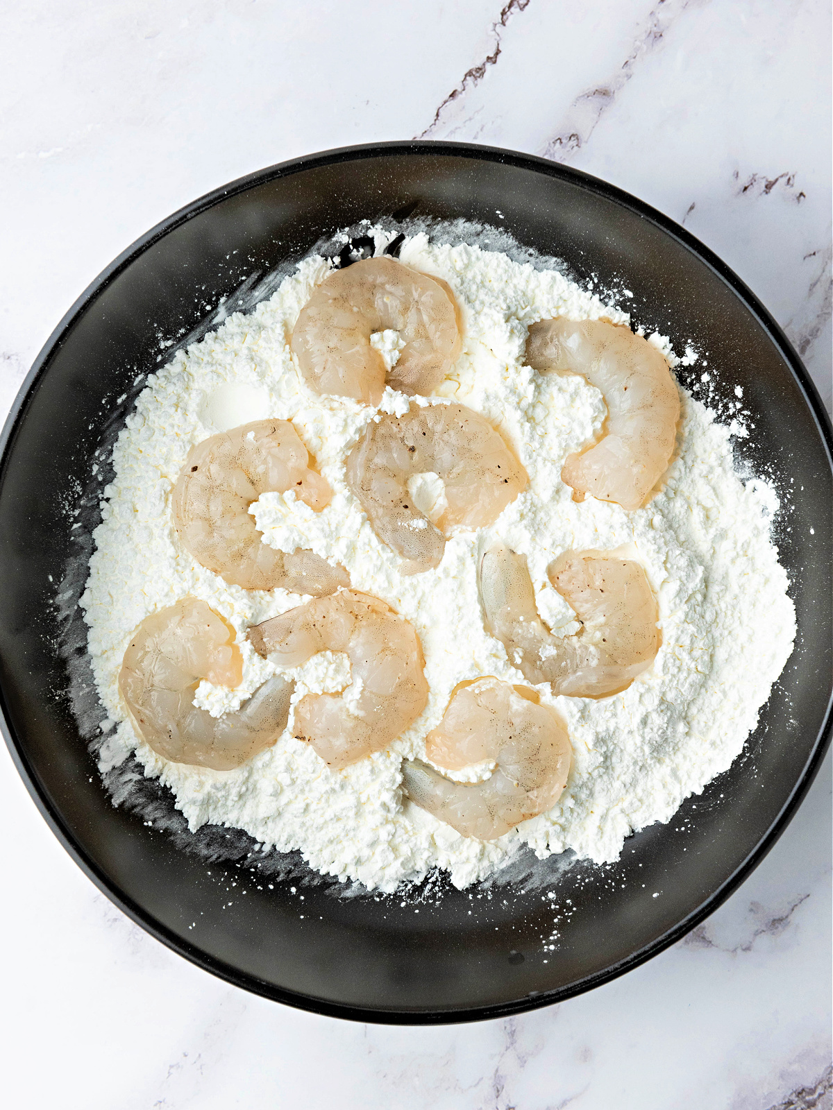 Raw shrimp being coated in a flour and cornstarch mixture.