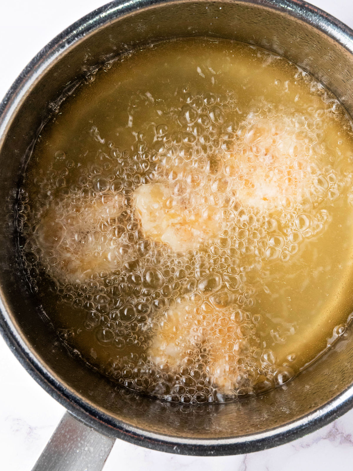 Shrimp frying in a pot of hot oil.