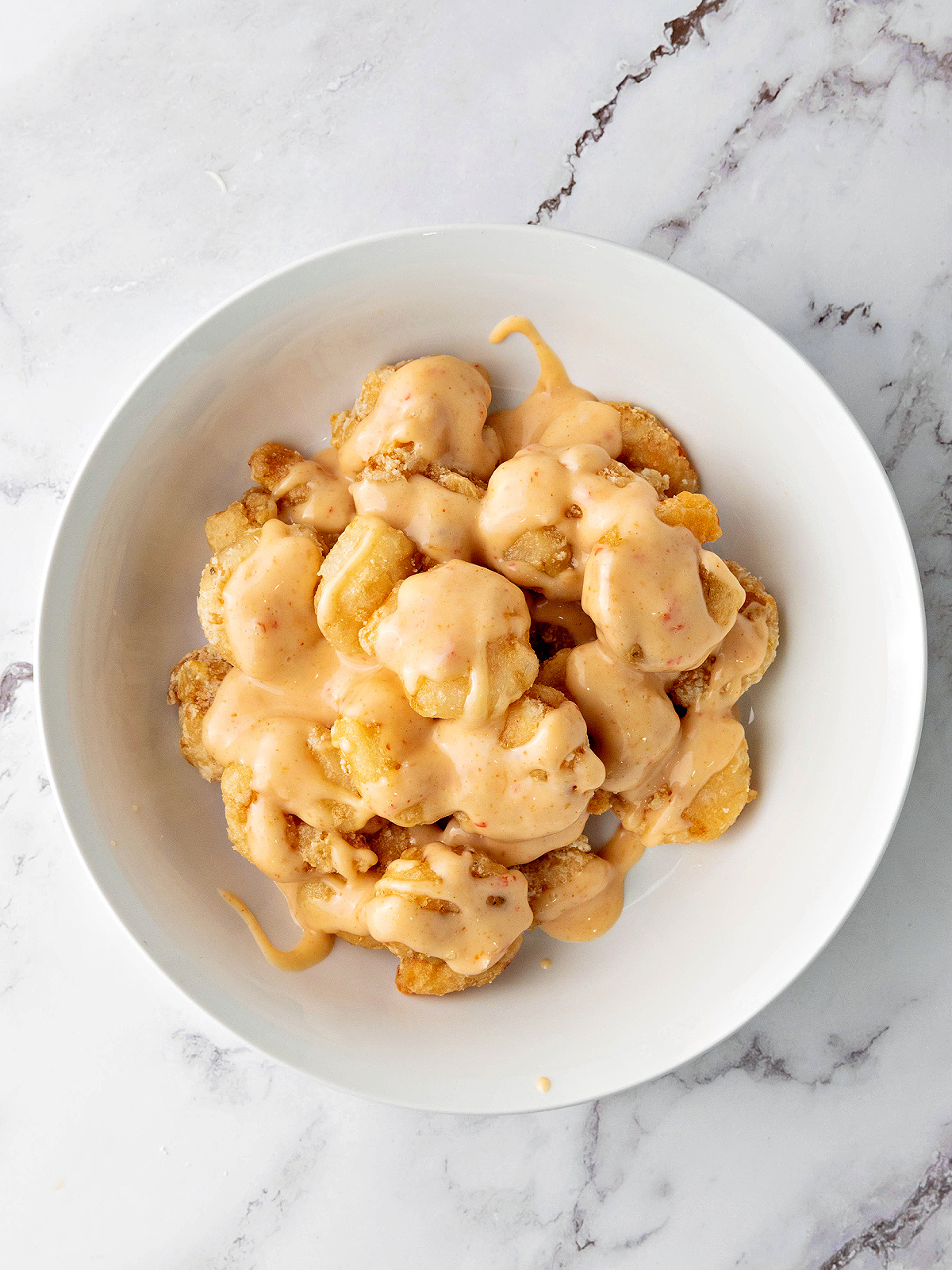 Fried shrimp being tossed in bang bang sauce.