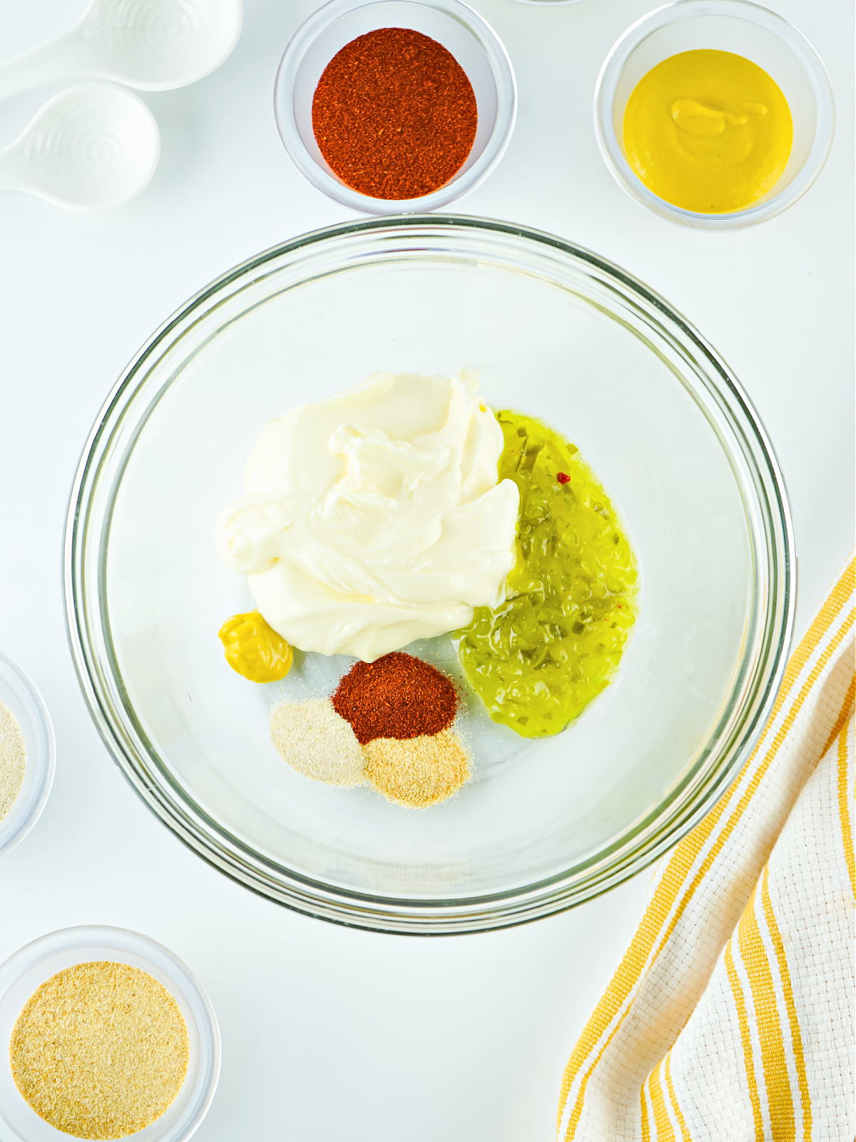 Mayonnaise, relish, mustard, and seasonings in a large glass mixing bowl.