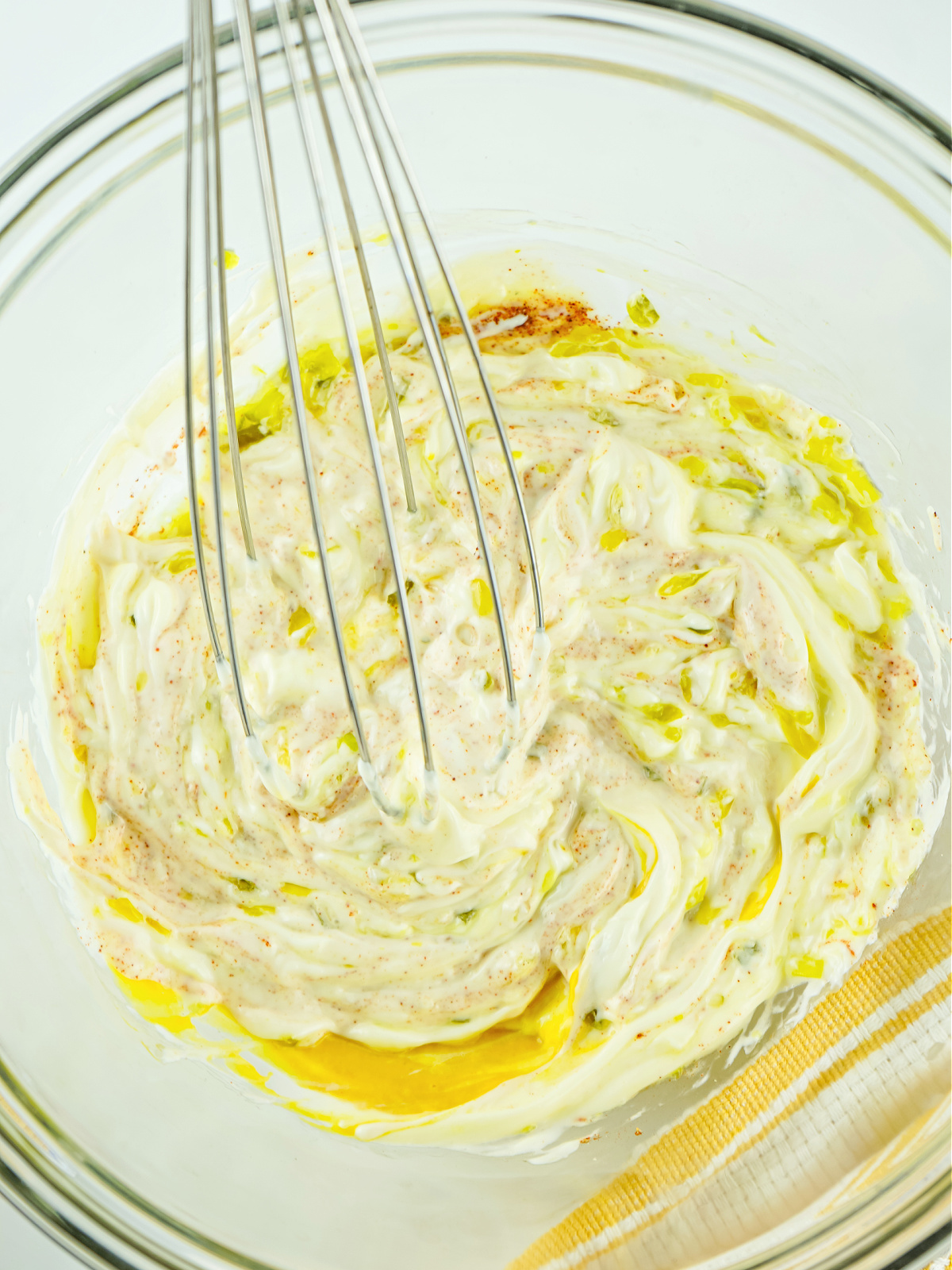 Mayonnaise, pickle relish, seasonings, and Dijon mustard being whisked in a bowl.