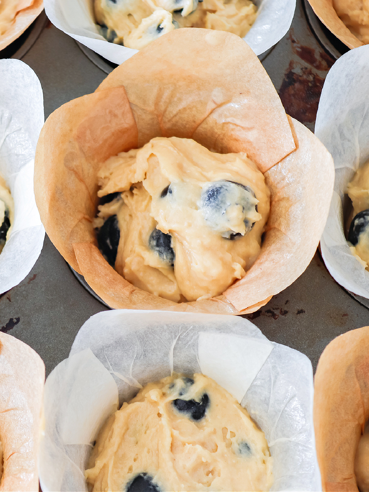 Blueberry muffin batter in a muffin tin waiting to be baked.