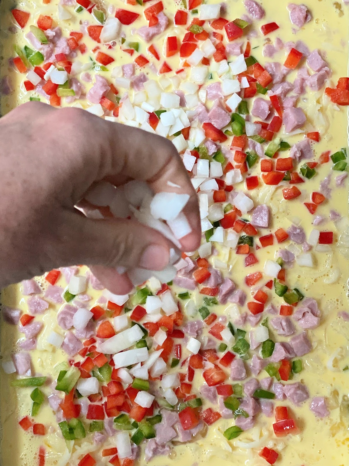 Woman sprinkling onions on top of a breakfast casserole.