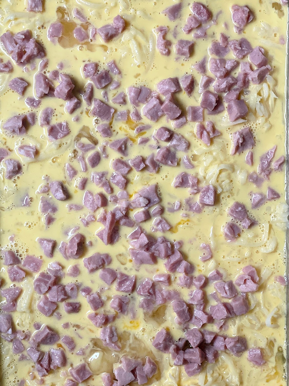 Ham cubes on top of egg mixture in a baking dish.