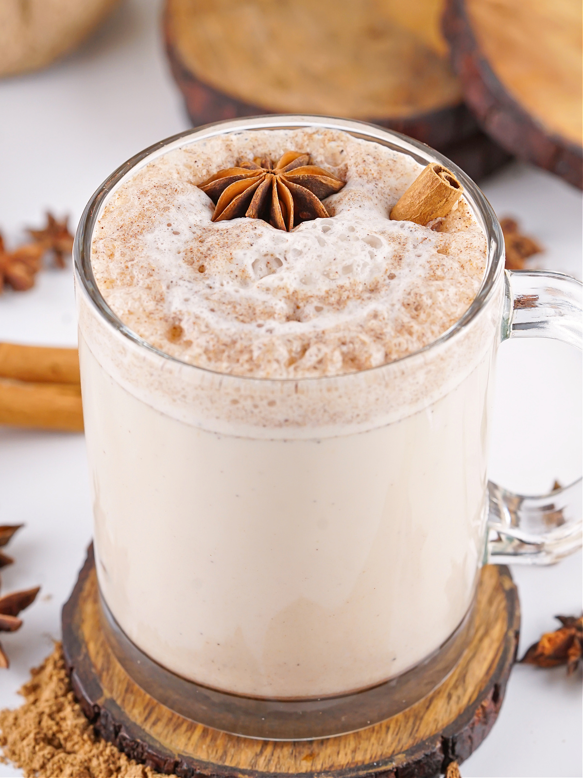 Chai latte in a glass mug topped with star anise and cinnamon stick.