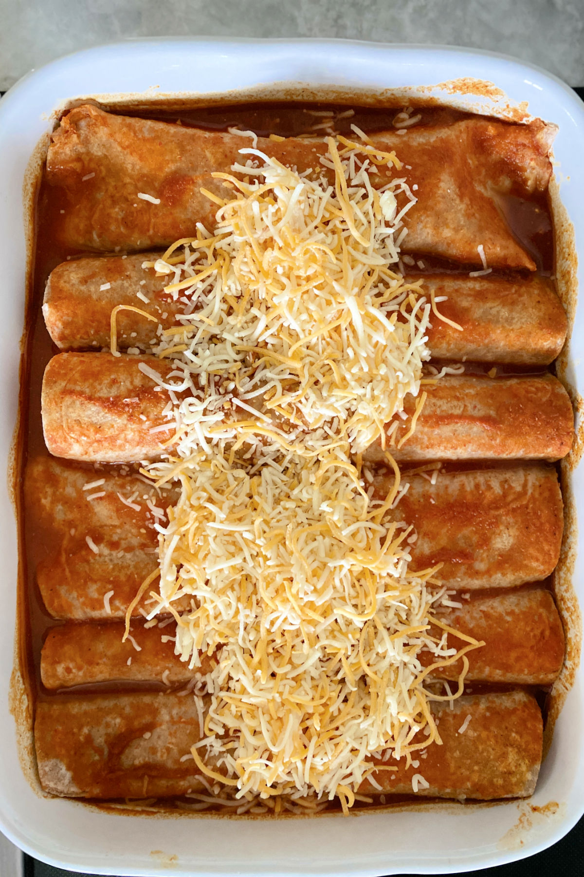 Shredded cheese on top of chicken enchiladas.