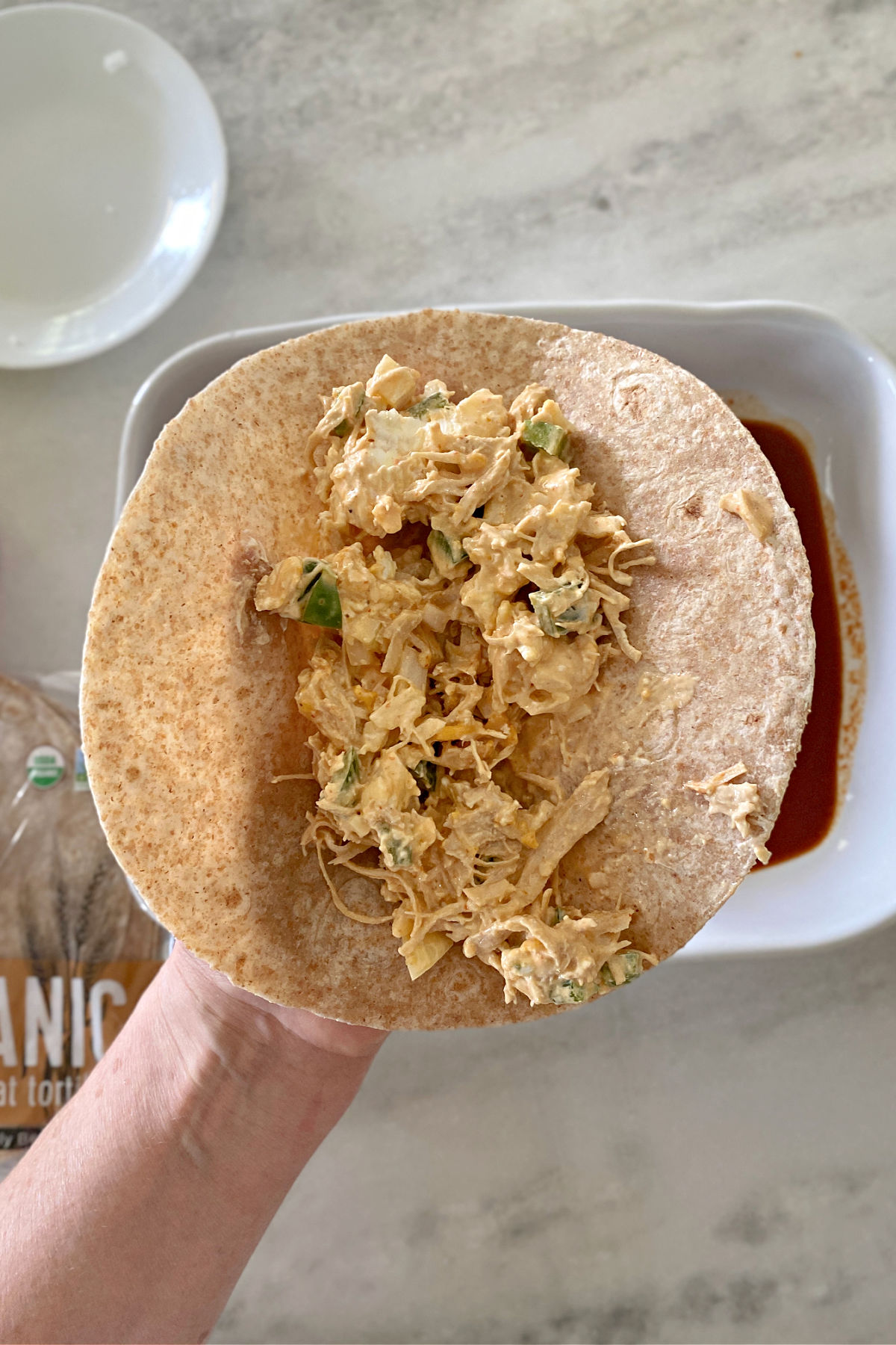 Chicken mixture on top of a tortilla about to be rolled up.