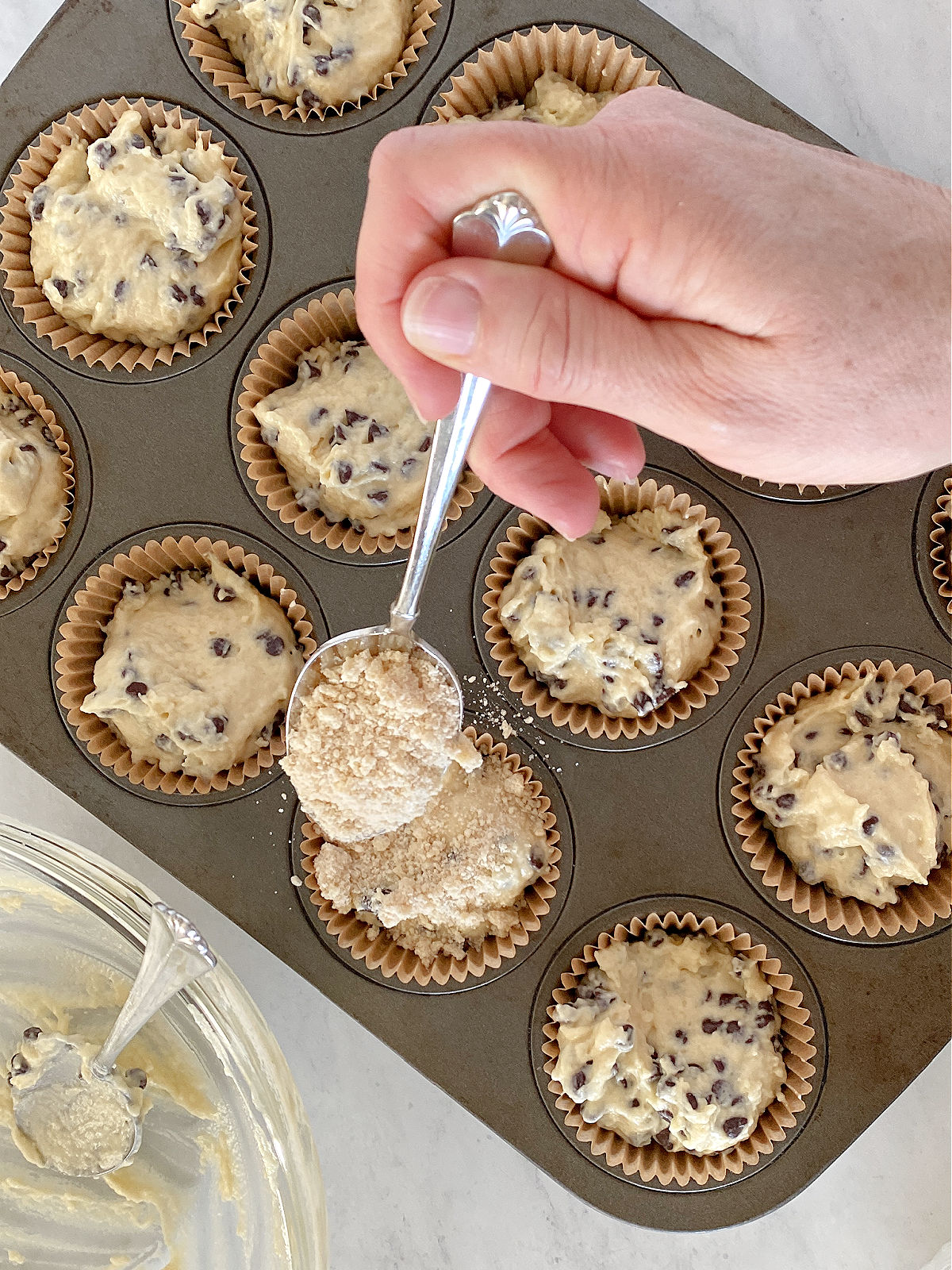 Crumbly topping being sprinkled over muffin batter.