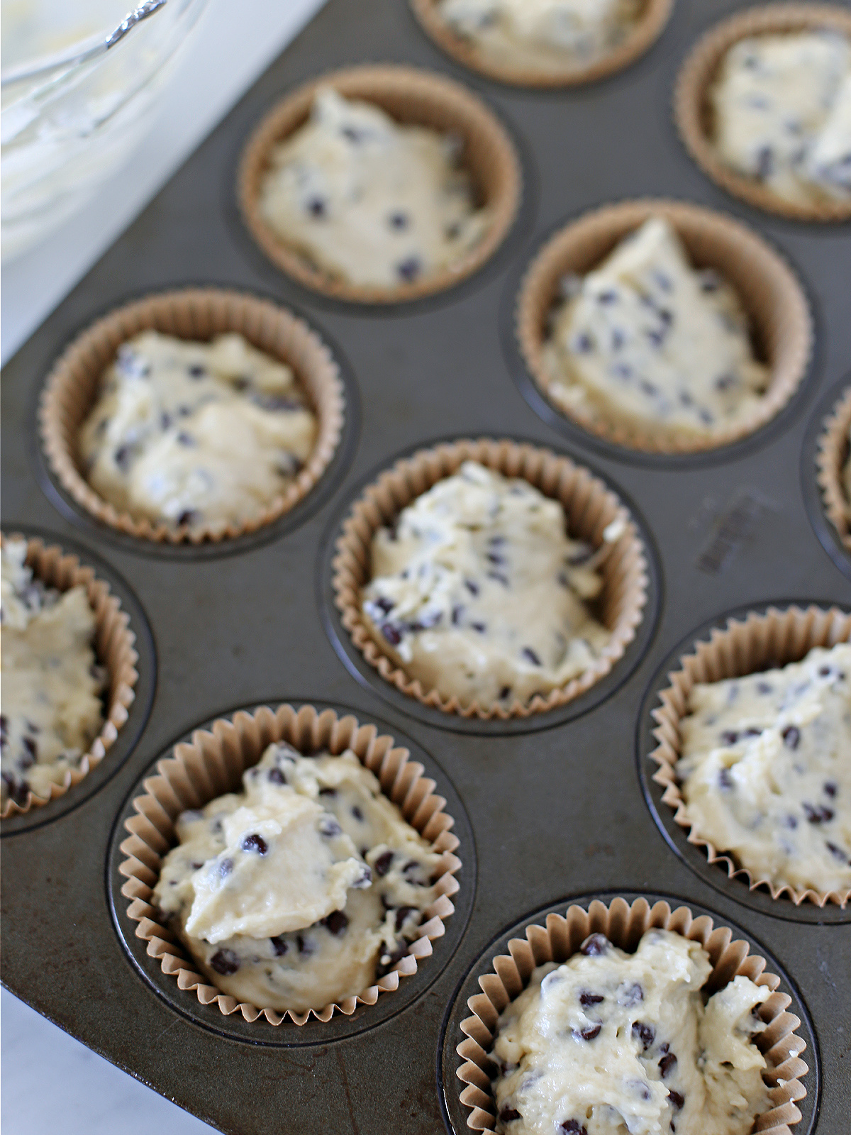 Chocolate chip muffin batter in a muffin pan.