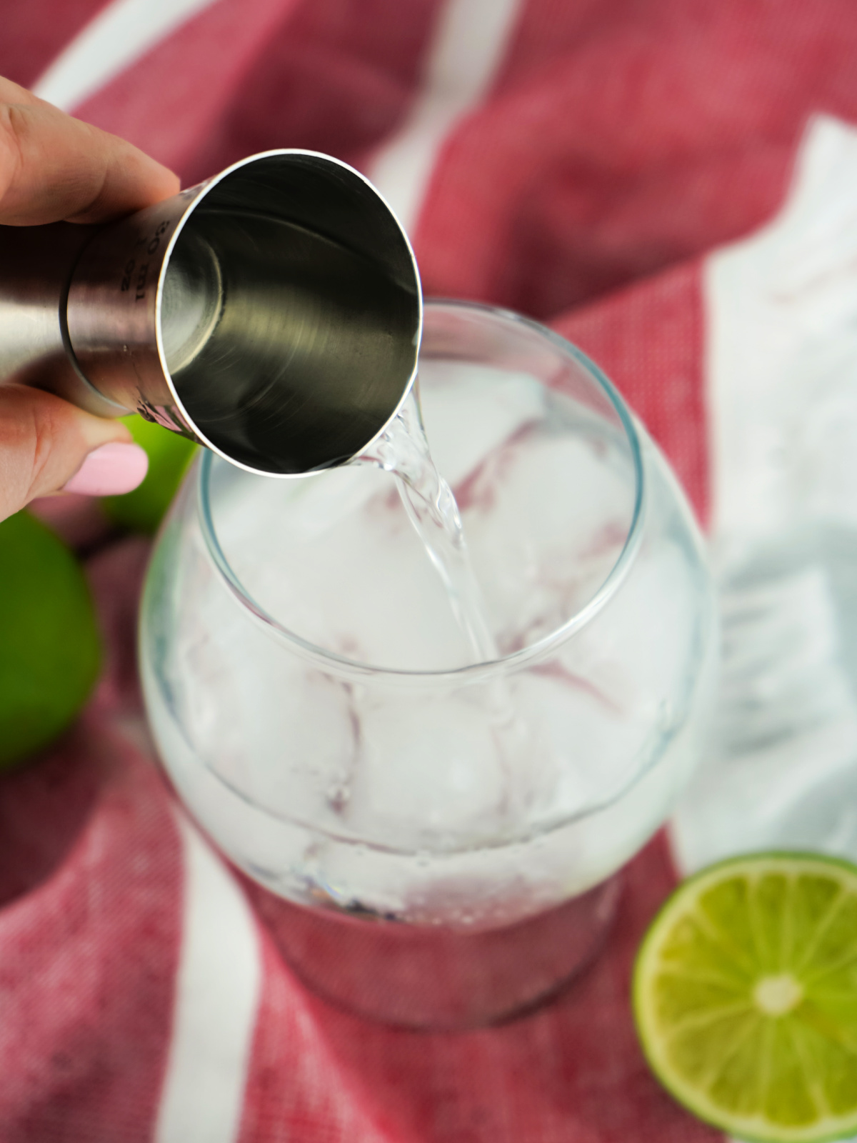 Vodka being poured into a large glass with ice.