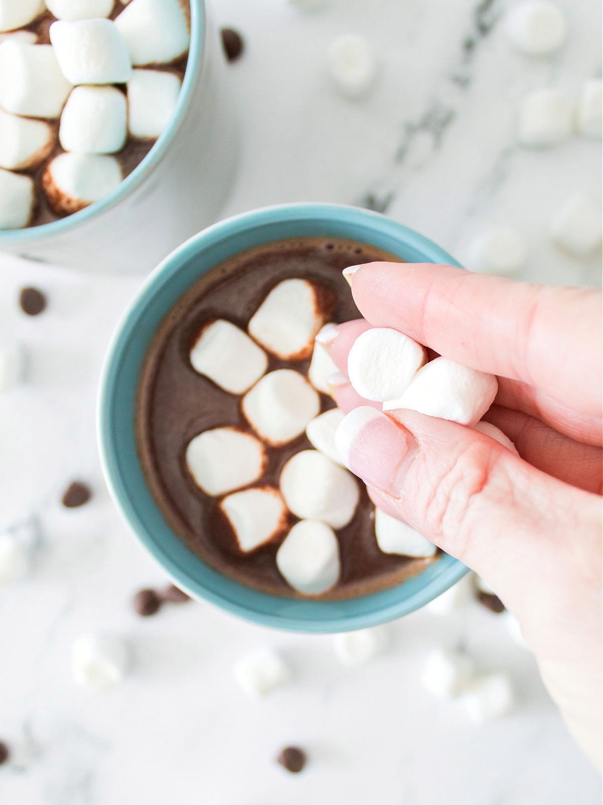 Topping a mug of hot chocolate with miniature marshmallows.