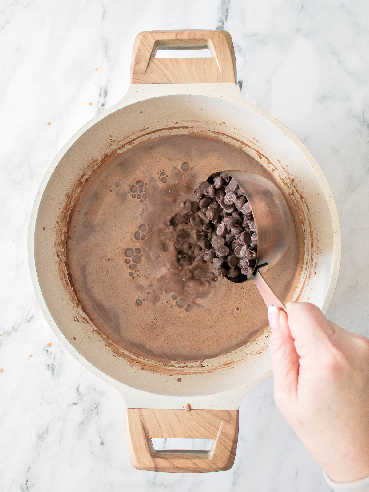 Adding chocolate chips to a pot with milk and cocoa powder.