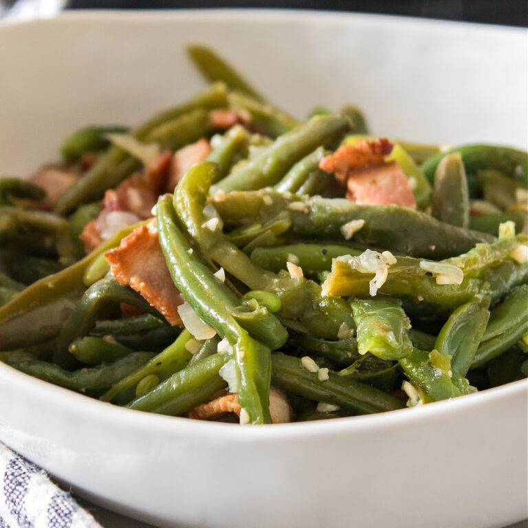 Bowl of green beans seasoned with garlic and bacon pieces.