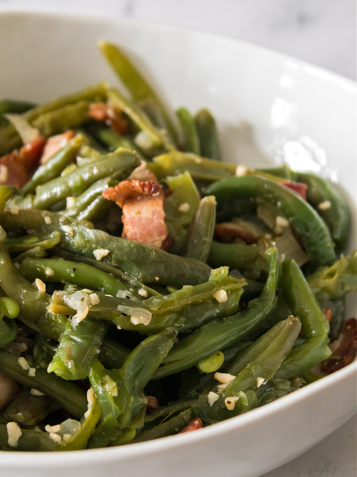 Bowl of green beans seasoned with garlic and bacon pieces.