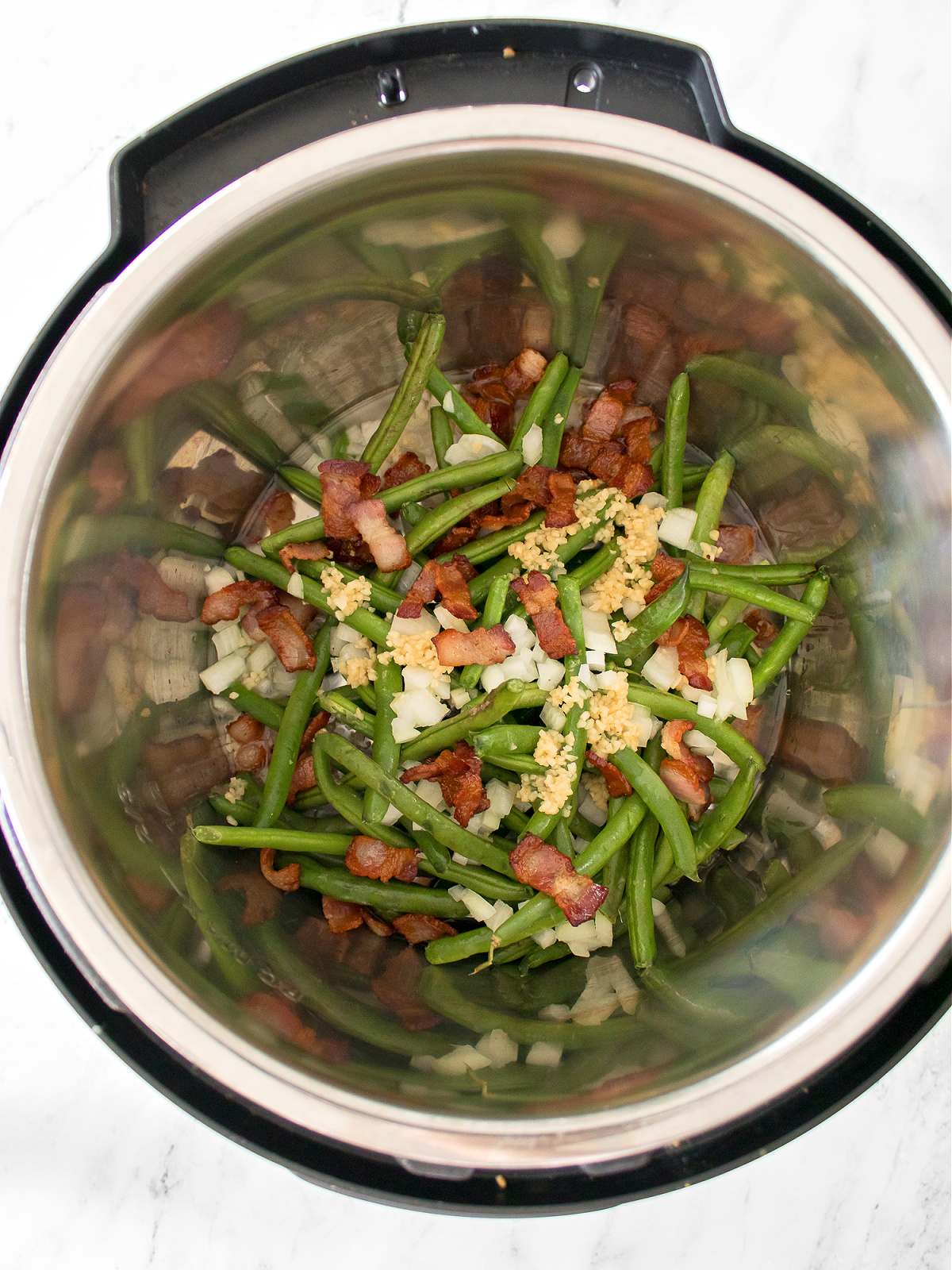 Green beans, onions, bacon, and seasonings in the bowl of an Instant Pot.