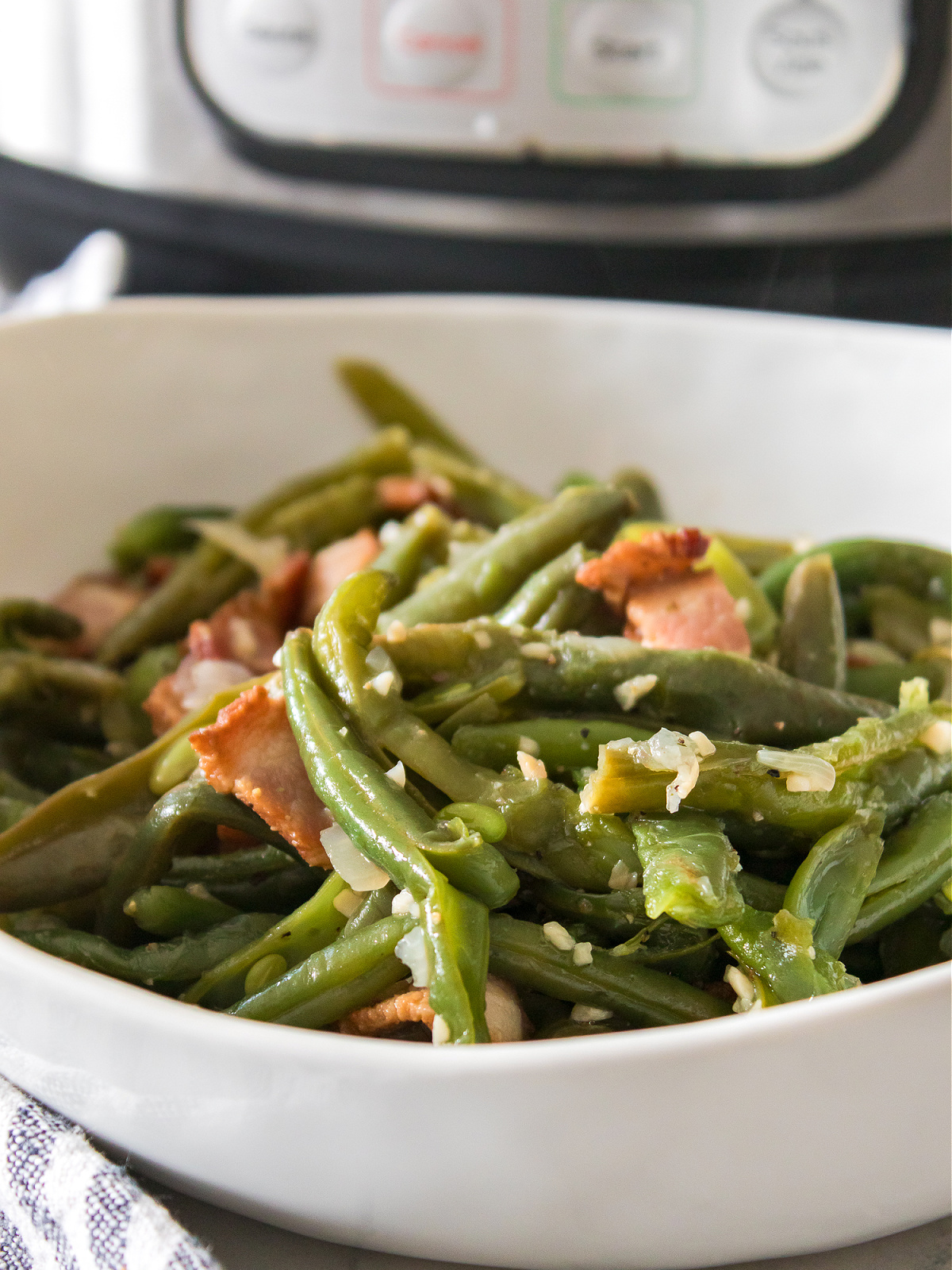 Green beans with seasoning and bacon in a white bowl in front of an Instant Pot.