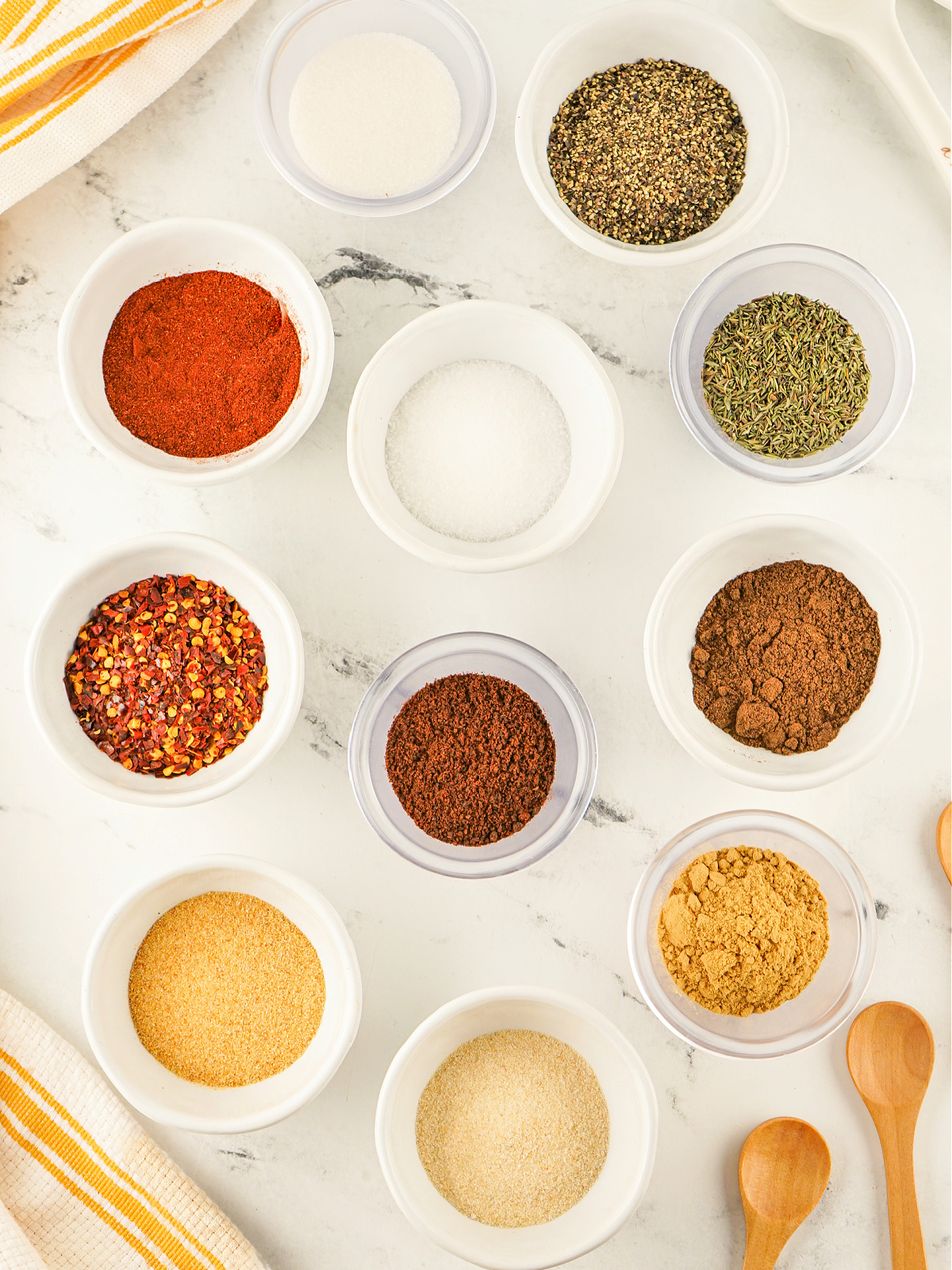 Small bowls of onion powder, garlic powder, crushed red pepper, black pepper, salt, paprika, allspice, sugar, ginger, clove, and thyme.