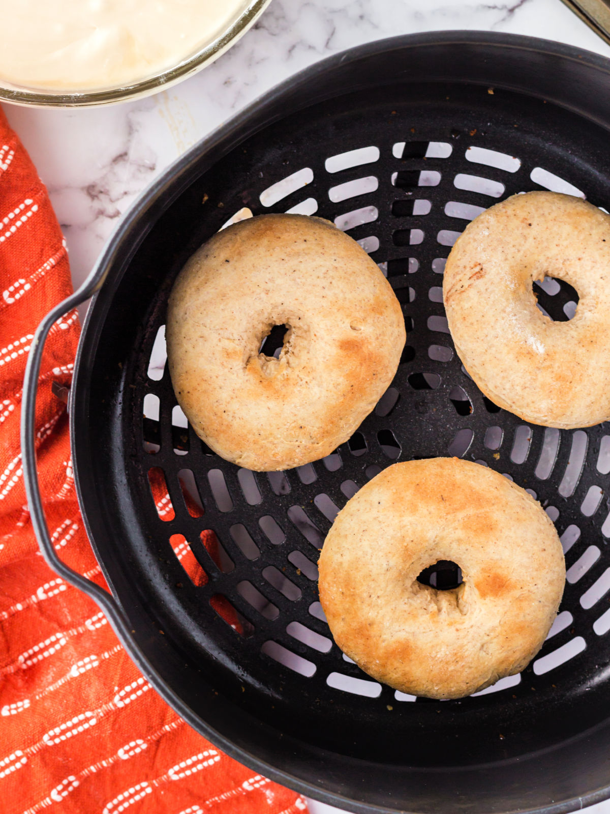 Three doughnuts in the basket of an air fryer.