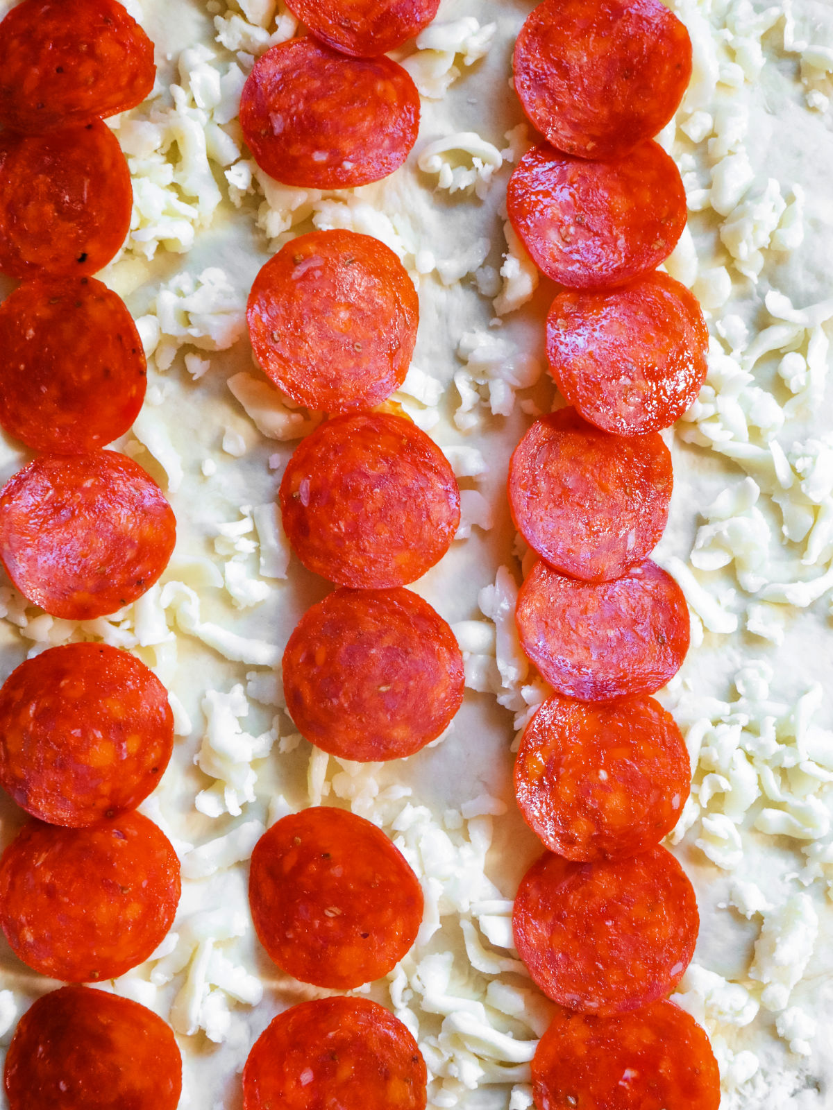 Rows of pepperoni and cheese on top of pizza dough.