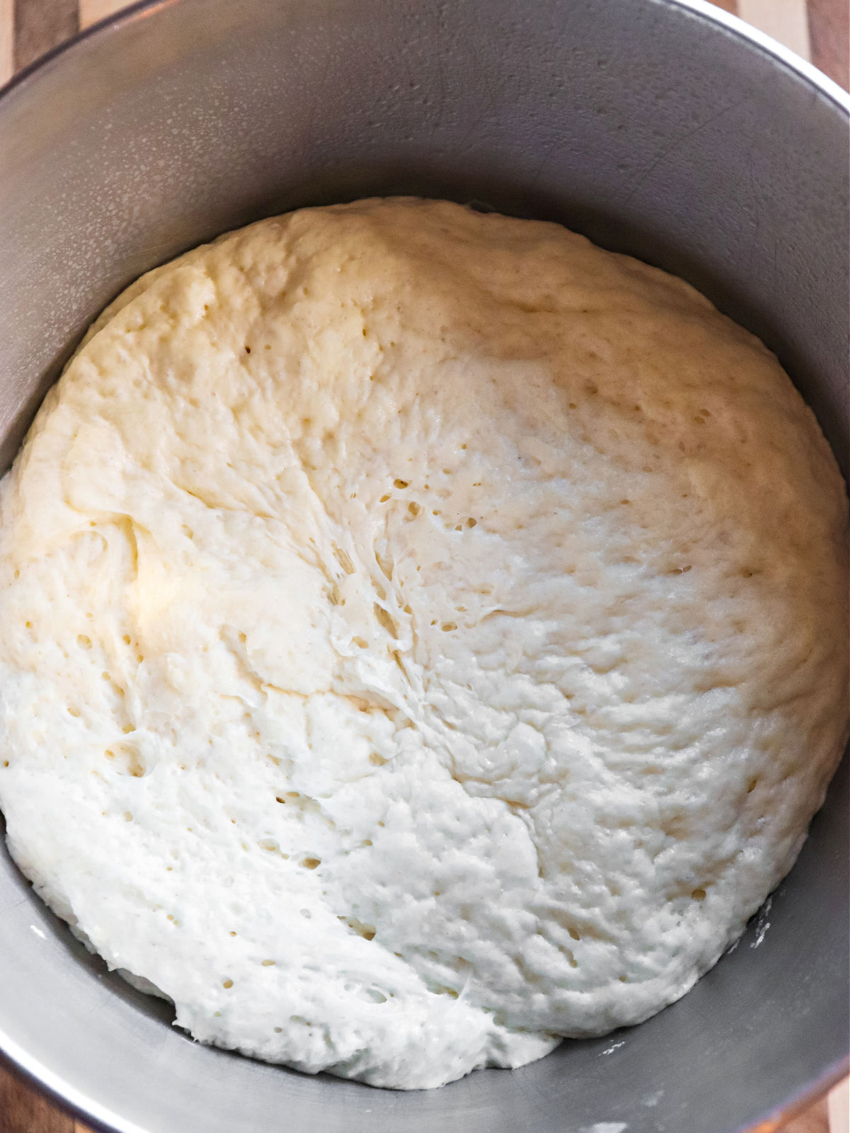 Risen pizza dough in a metal bowl.