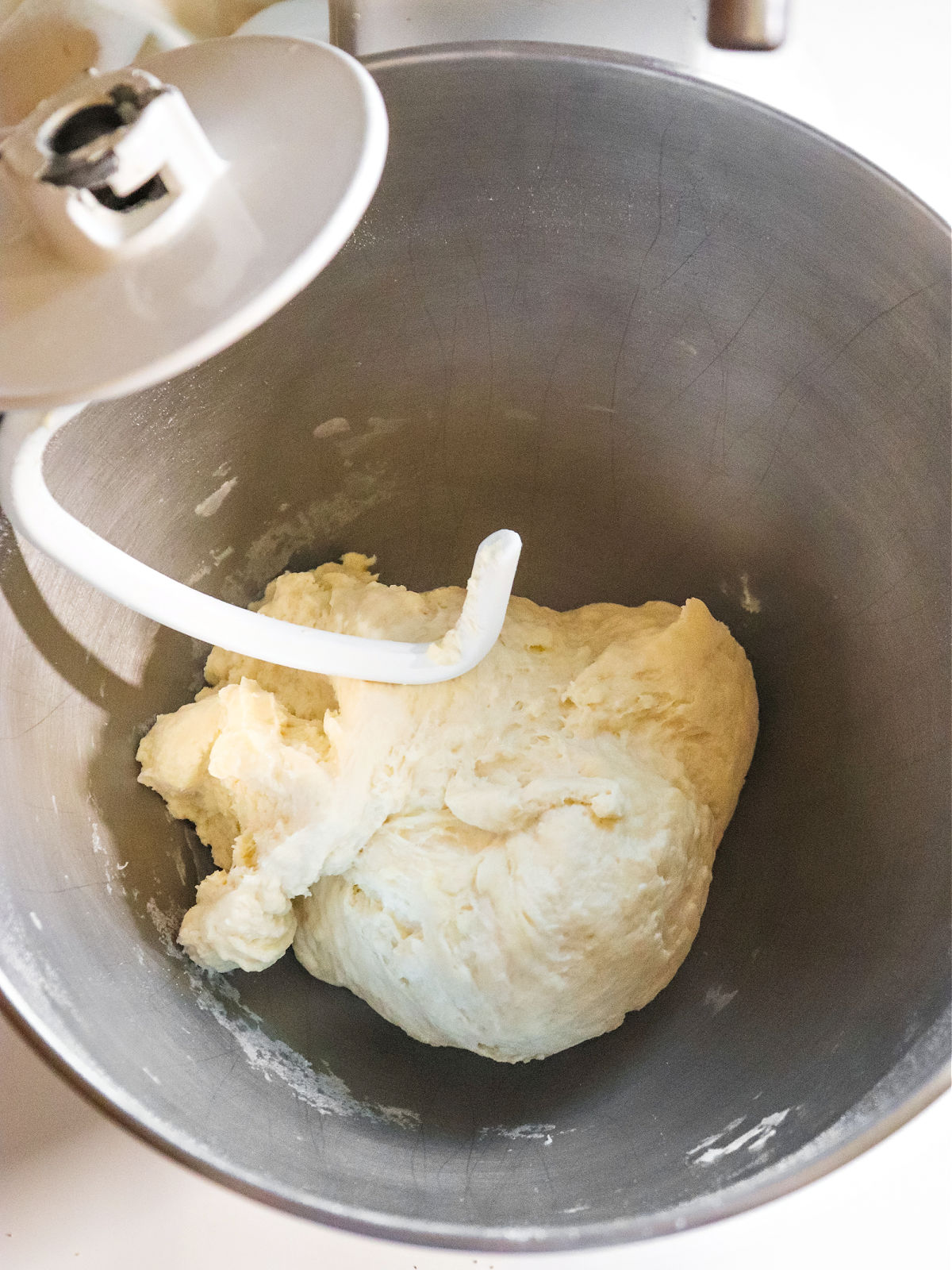 Pizza dough in the bottom of a metal mixer bowl.