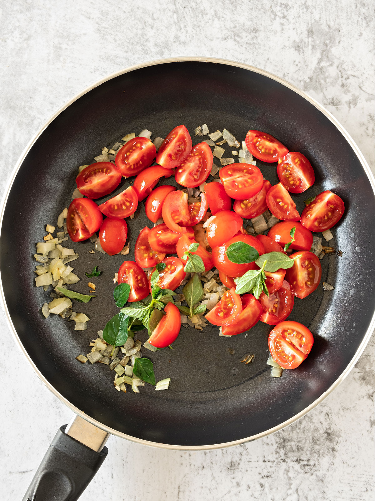 Cherry tomatoes and onions cooking in a skillet.