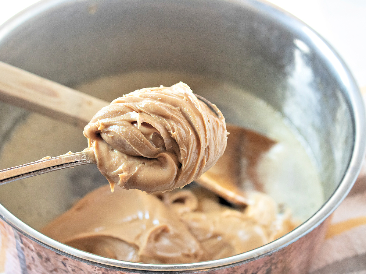 Scoop of peanut butter about to be added to a saucepan.