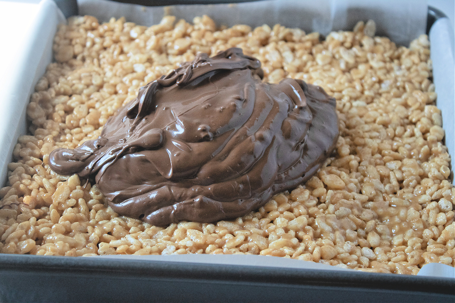 Melted chocolate on top of peanut butter Rice Krispies in a pan.