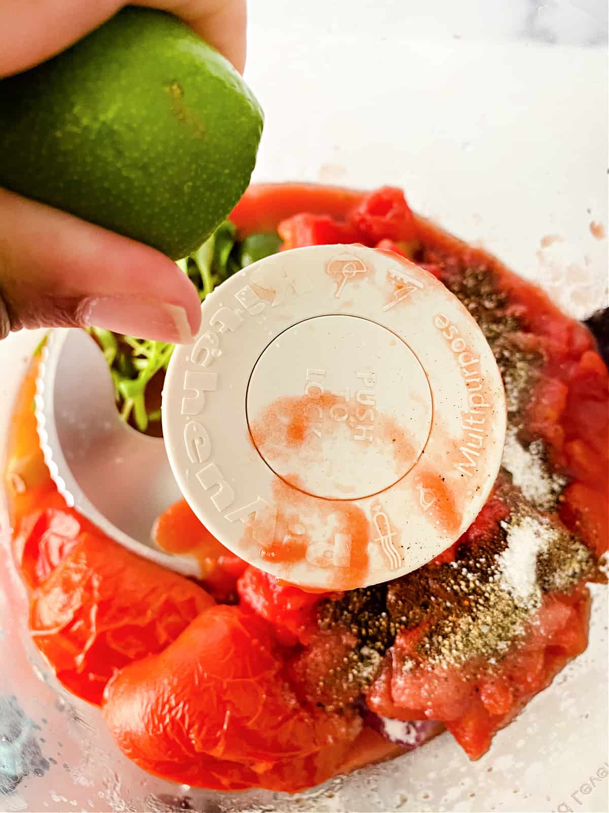 Lime being squeezed into tomatoes in a food processor.