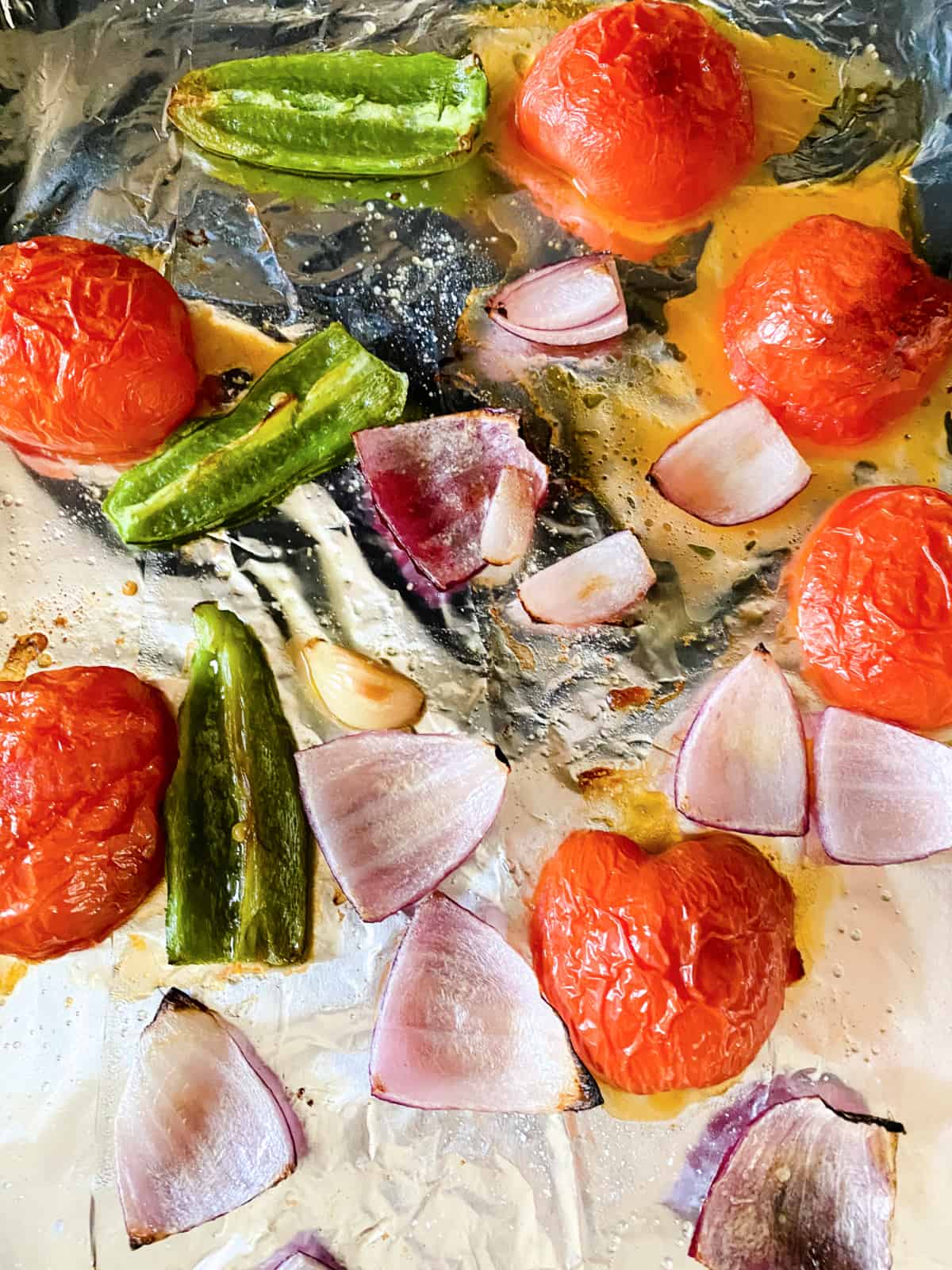 Roasted vegetables and tomatoes on a baking sheet lined with aluminum foil.