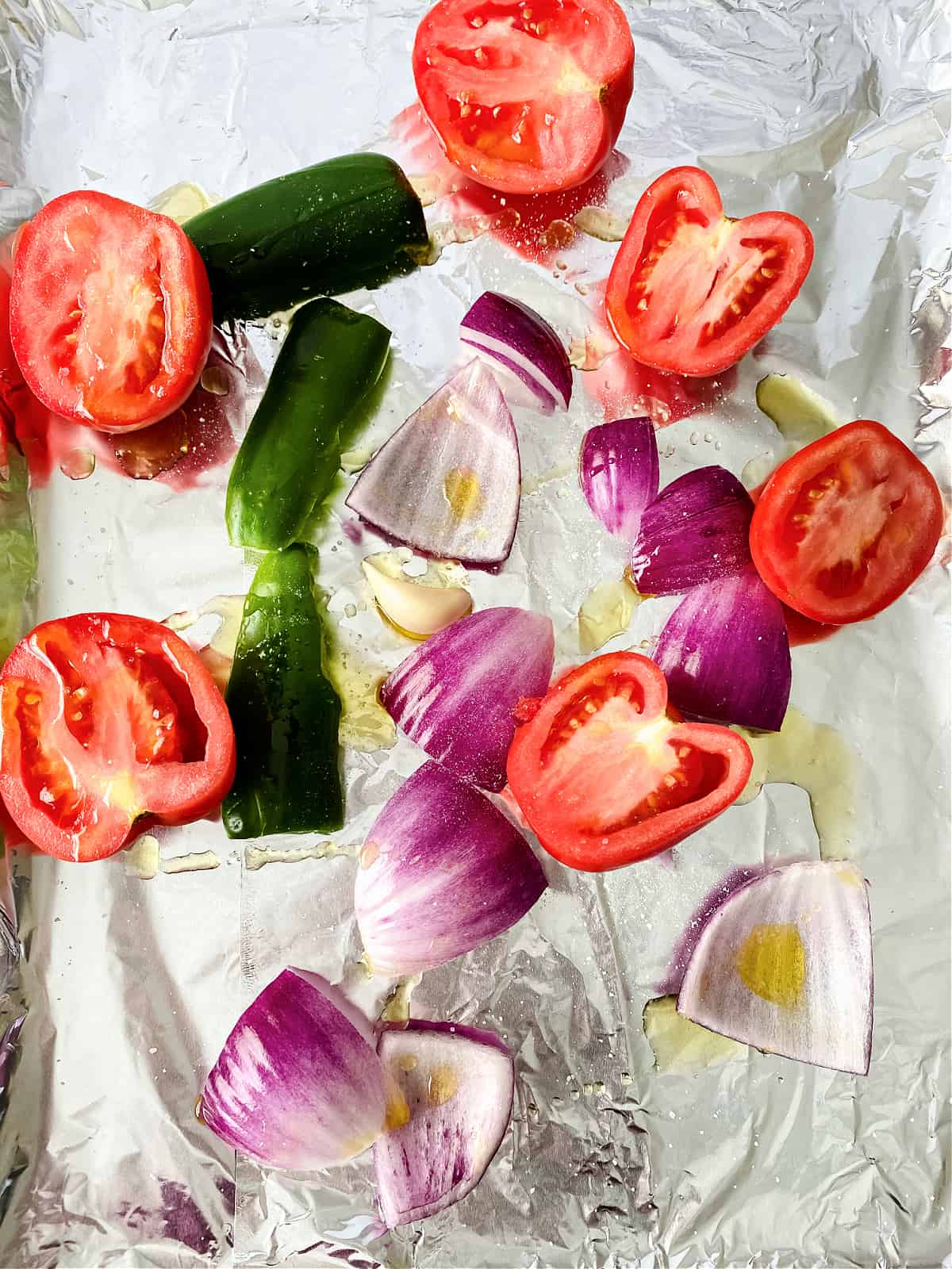 Tomatoes, jalapenos, and onions drizzled with oil on a baking sheet.