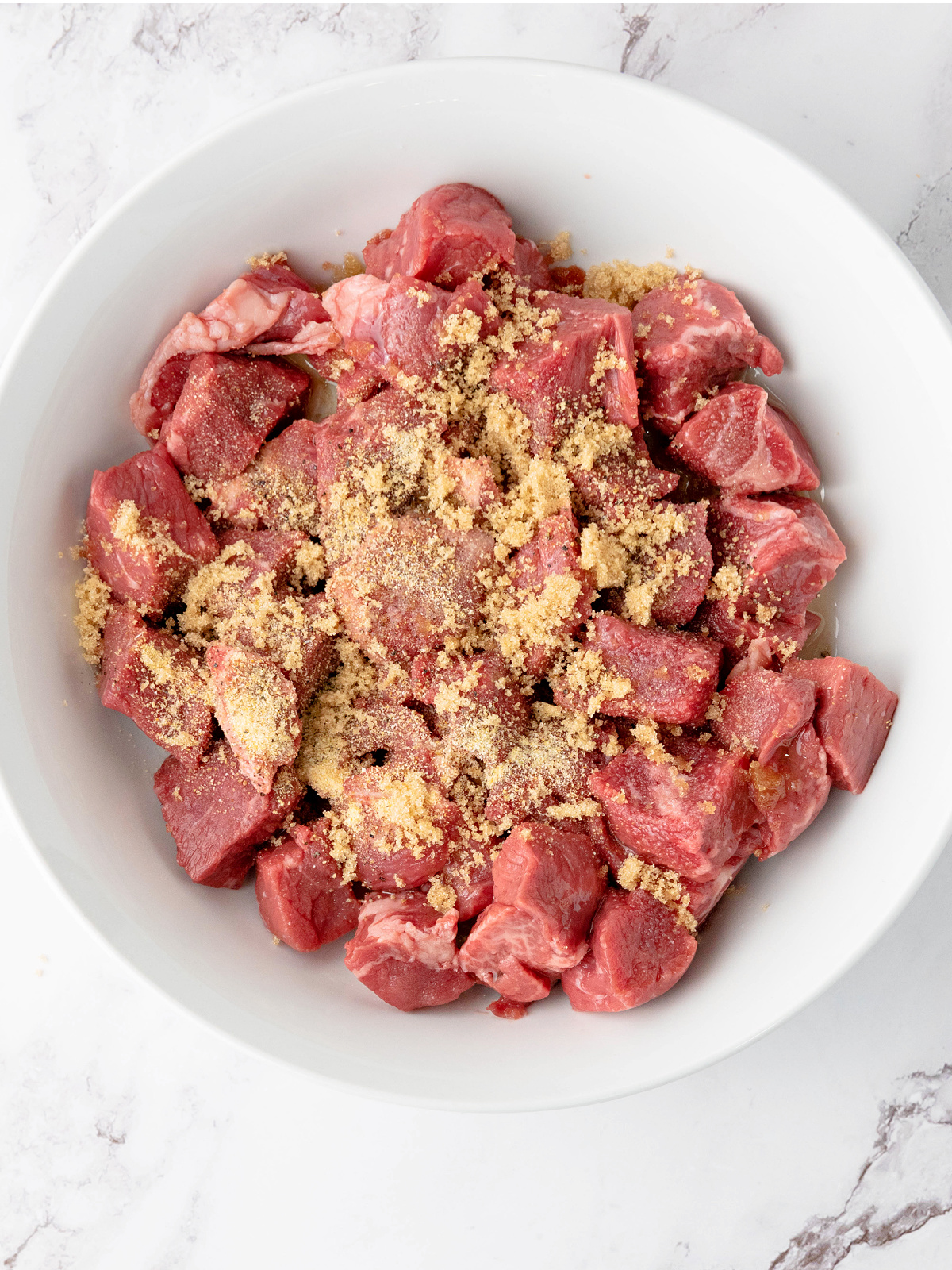 Seasoning on top of steak cubes in a bowl.