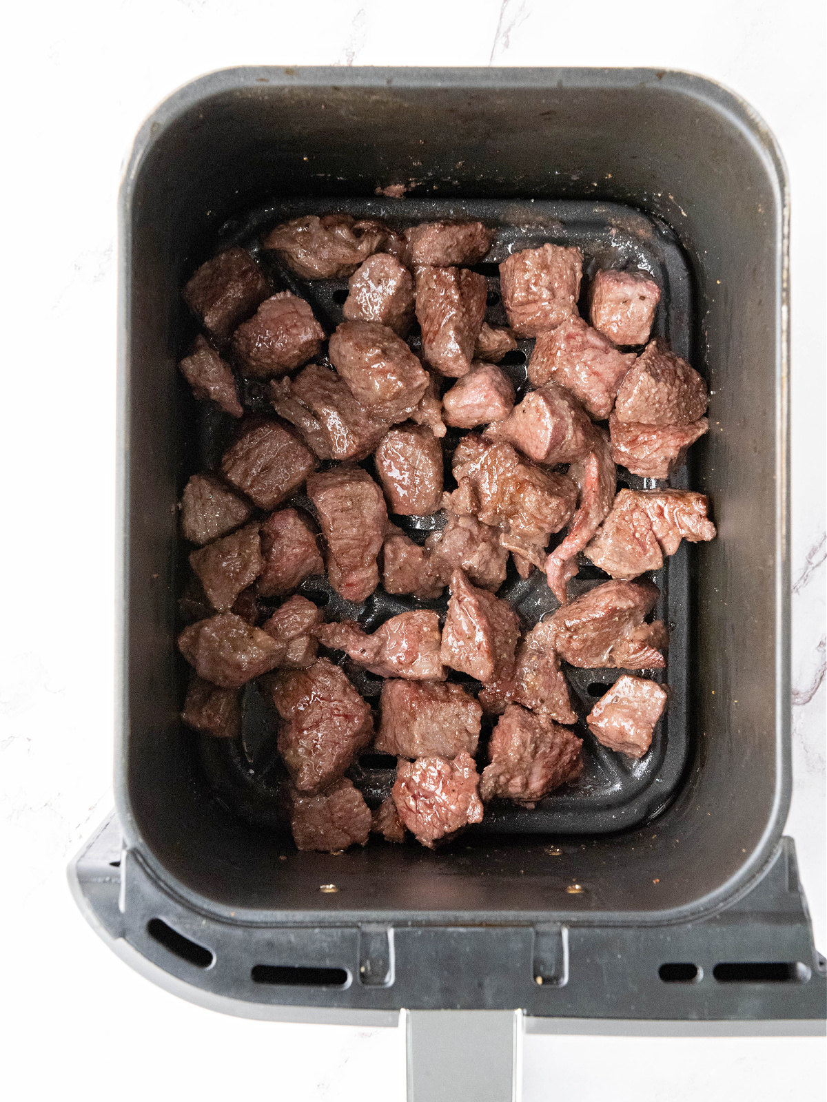 Cooked steak cubes in an air fryer basket.