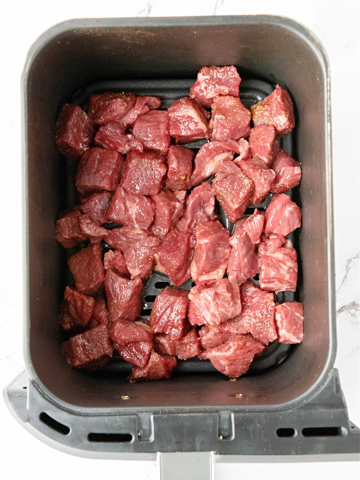 Raw seasoned beef cubes in an air fryer basket.