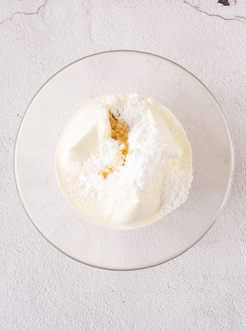 Mascarpone cheese, vanilla, heavy cream, and powdered sugar in a bowl.