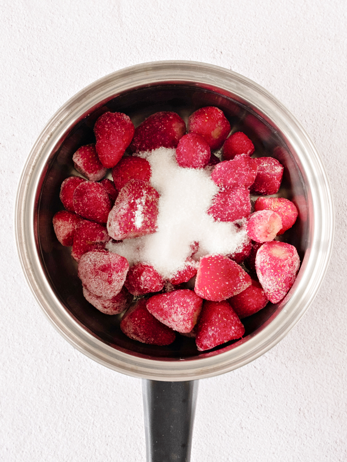 Strawberries and sugar in a small pot.