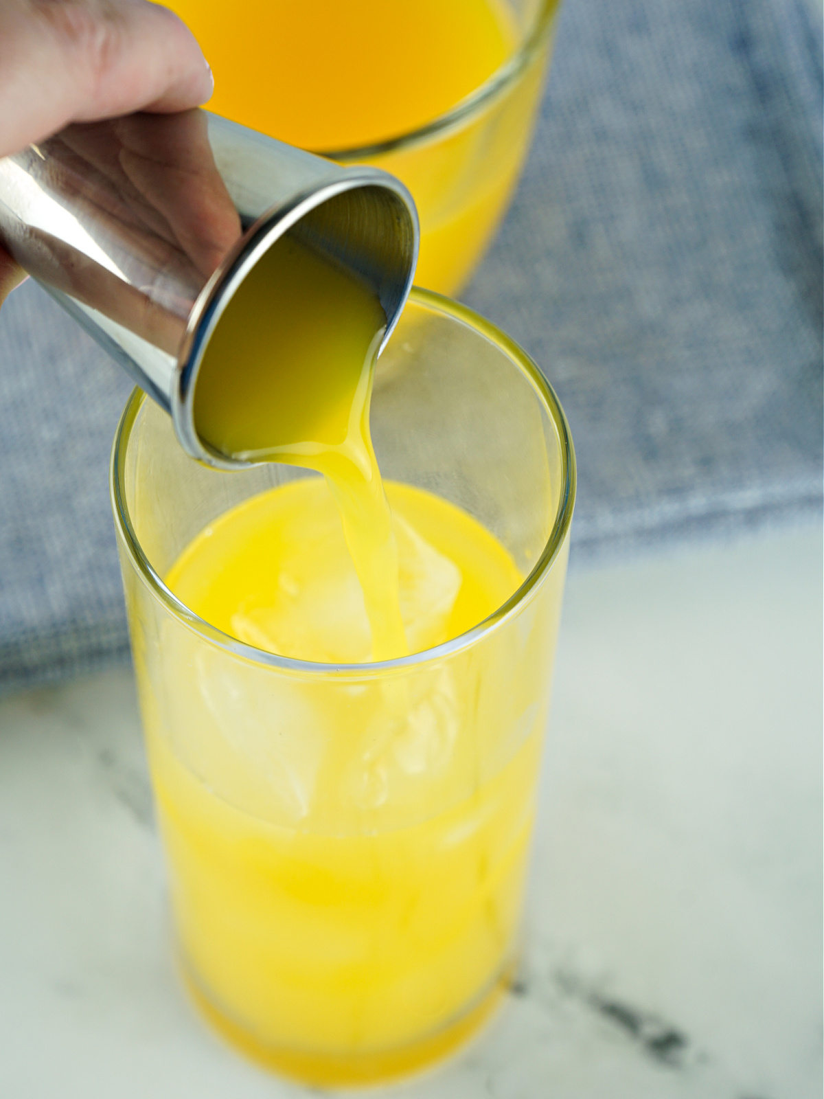 Orange juice being poured into a glass filled with ice.