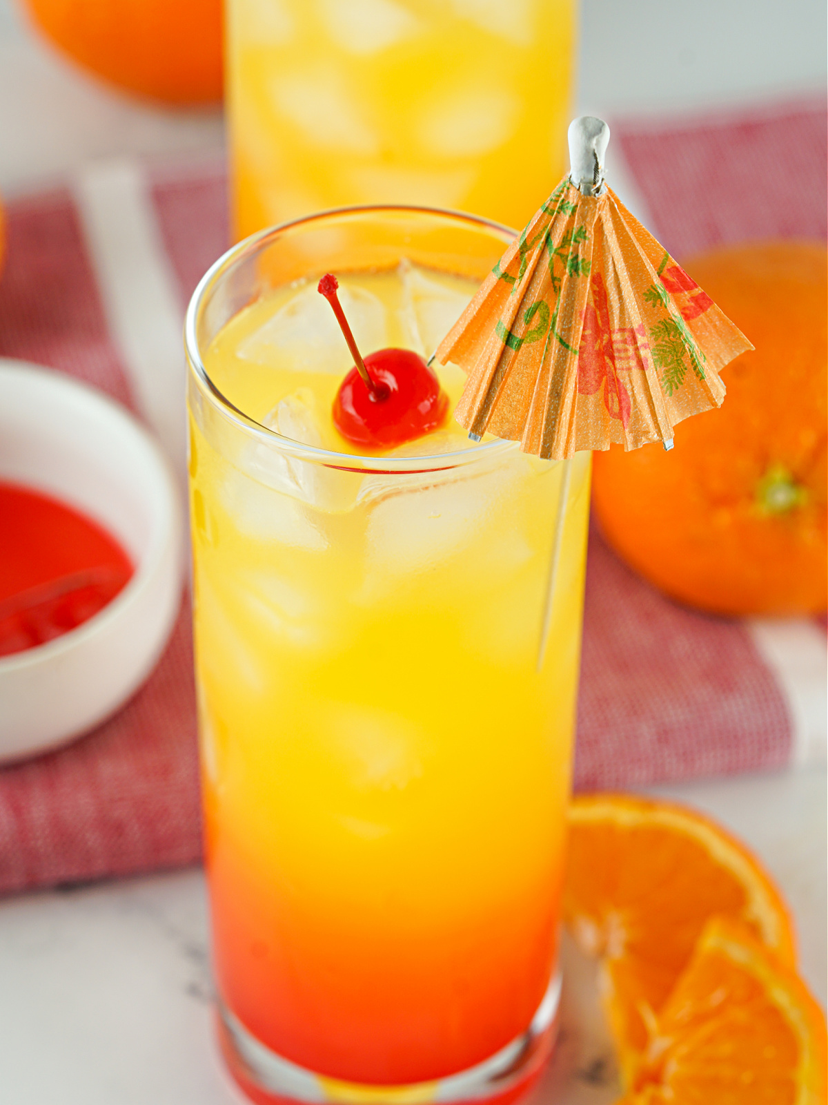 Tequila Sunrise in a glass and garnished with a small umbrella.