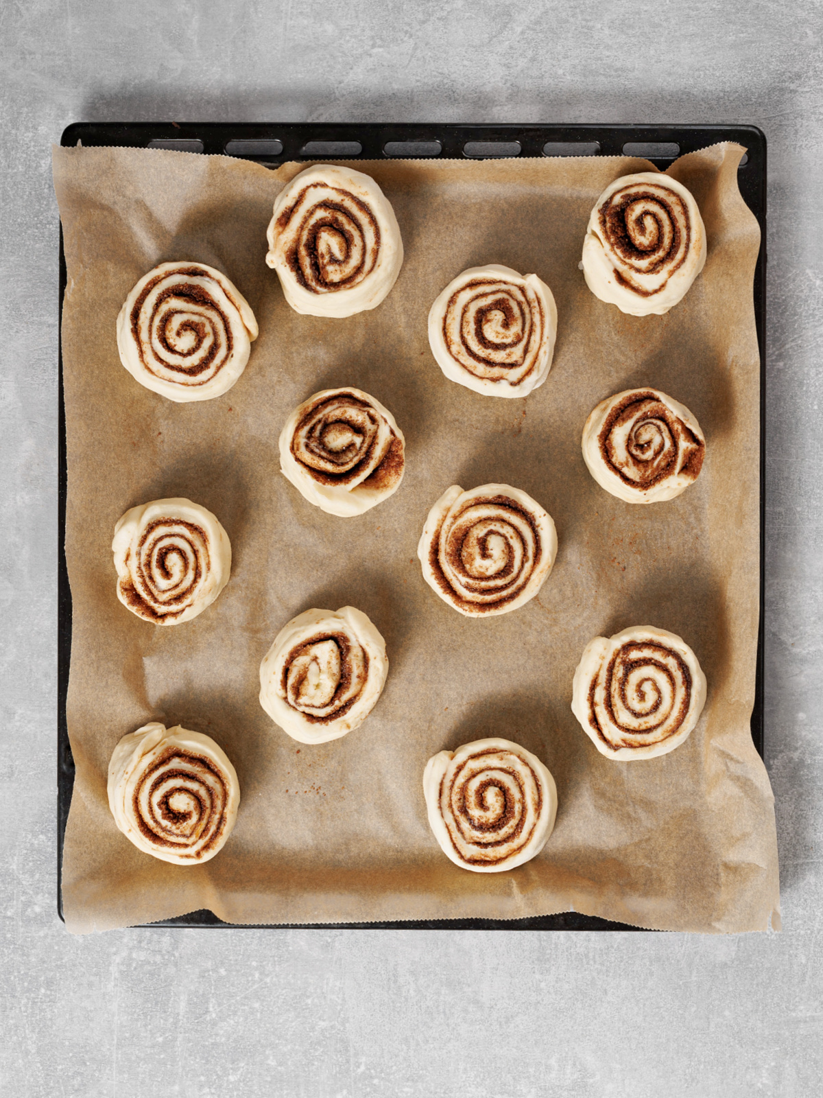 Cinnamon rolls on a piece of parchment paper in a pan.