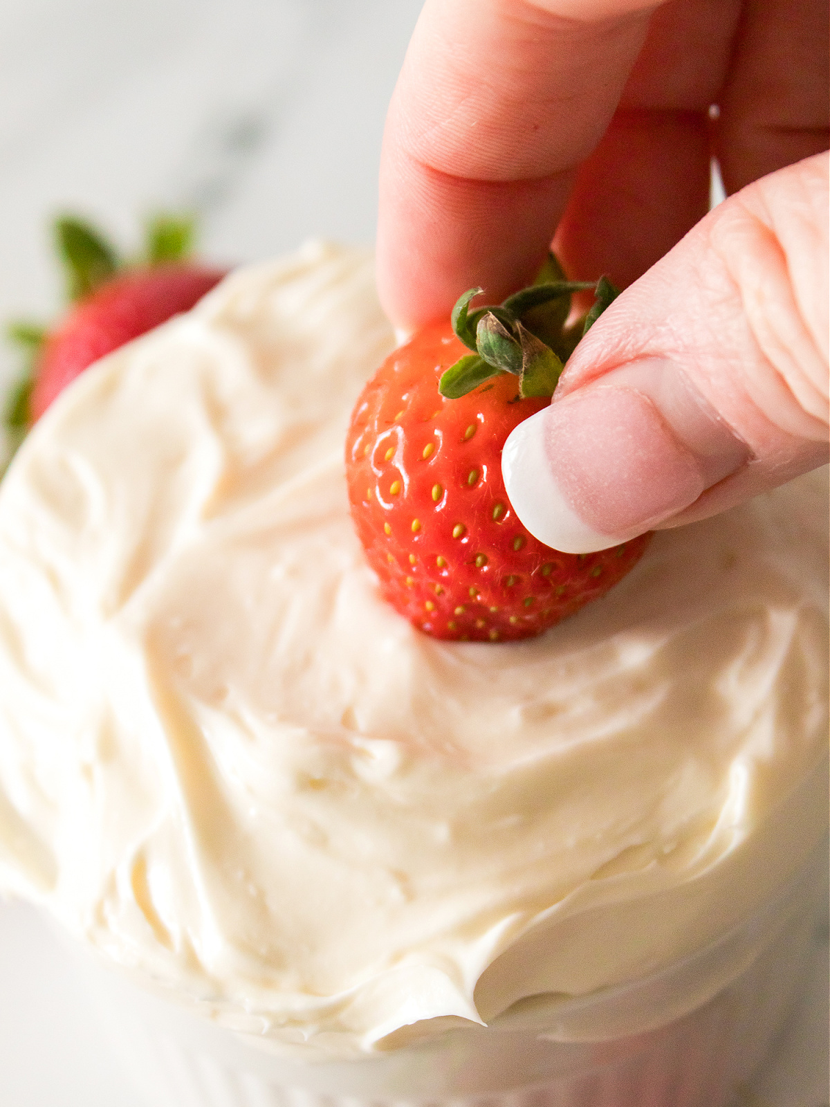 A fresh strawberry being dipped into a creamy fruit dip.