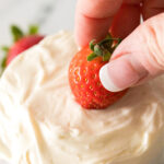 A fresh strawberry being dipped in a creamy fruit dip.