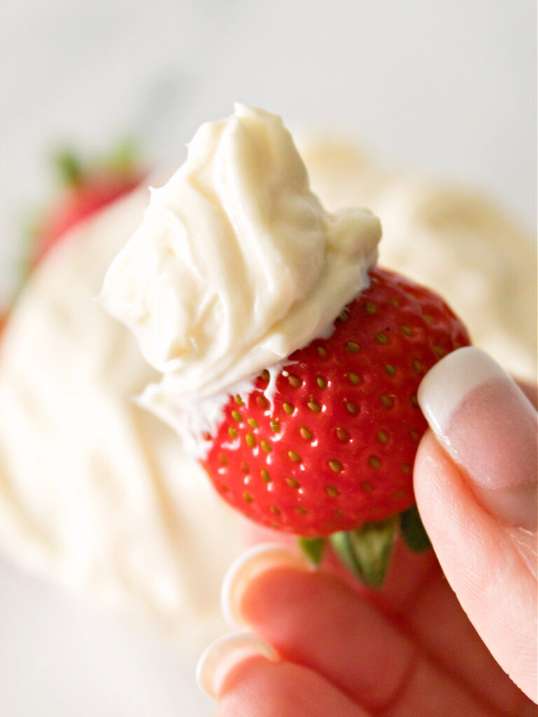 Woman's hand holding a strawberry that has been dipped in a creamy fruit dip.