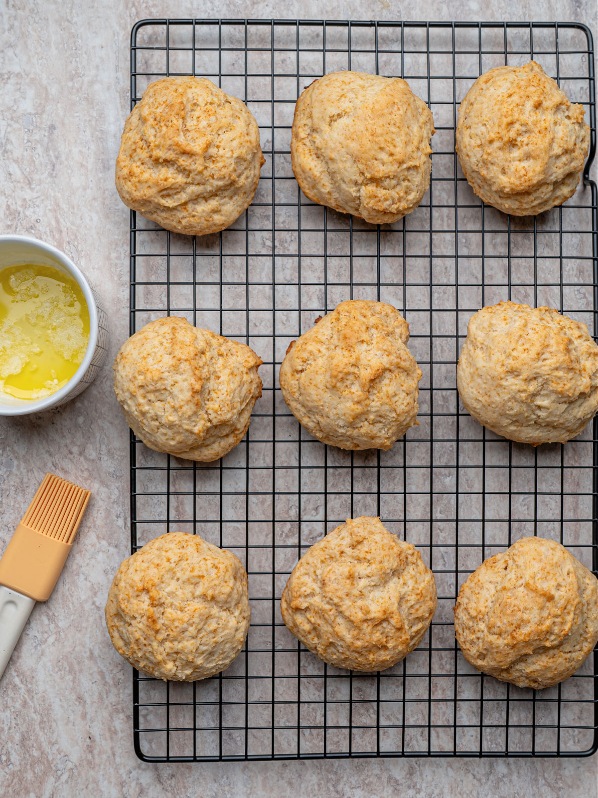 Baked biscuits on a wire rack beside a small bowl of melted butter.