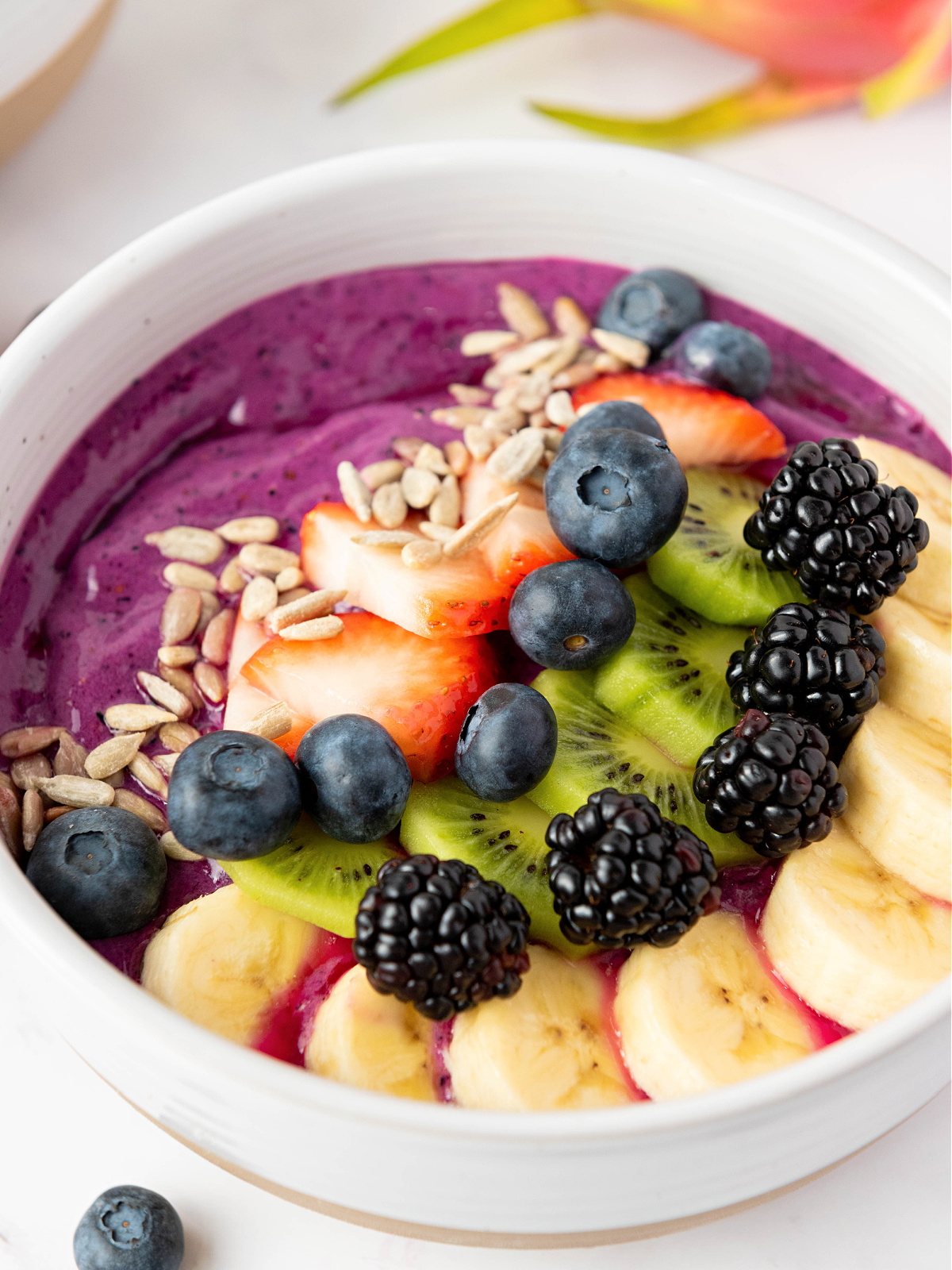 Smoothie bowl made with dragon fruit and topped with fresh berries, kiwi, and bananas.