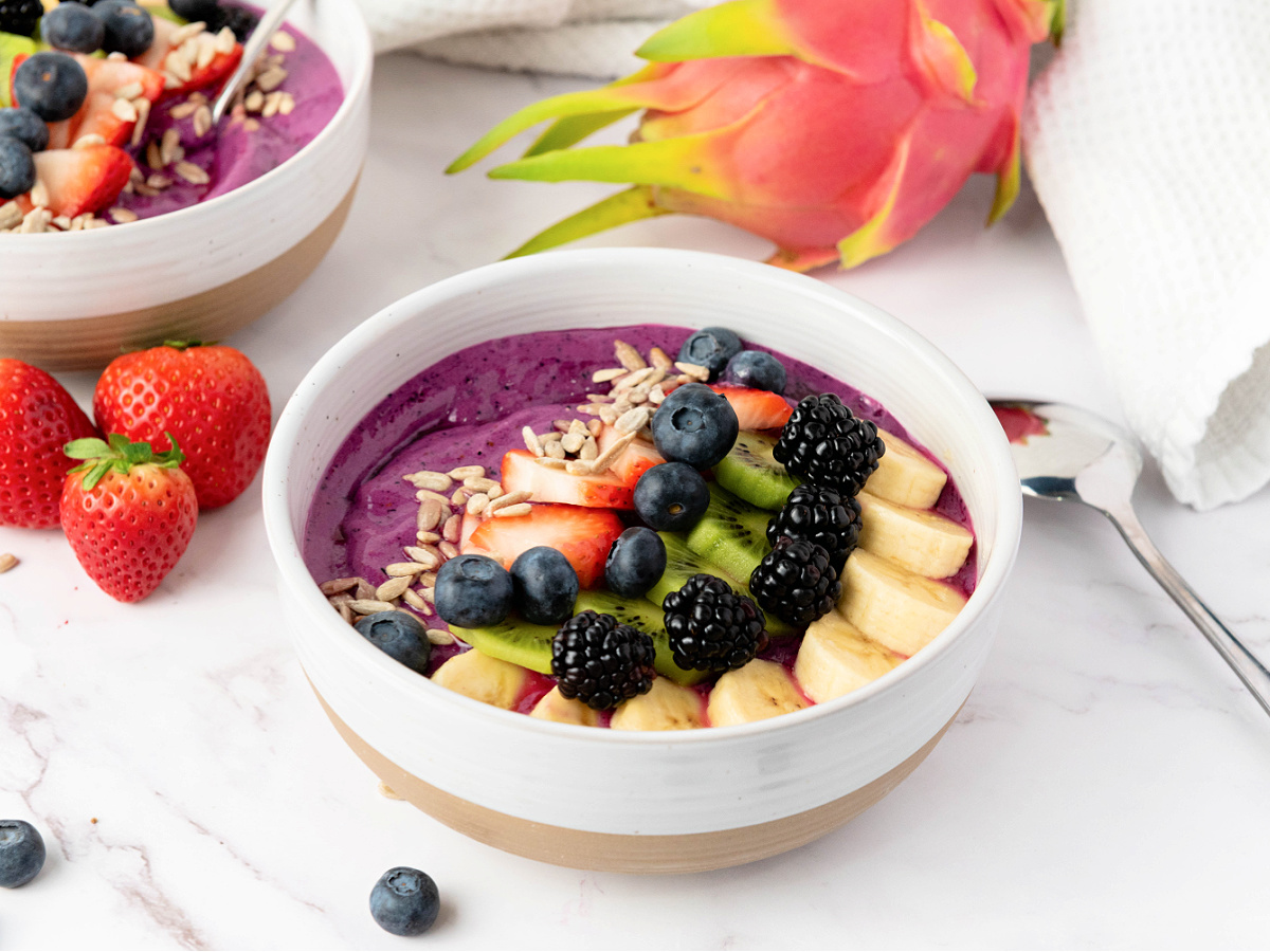 A smoothie bowl topped with sunflower seeds, fresh strawberries, blueberries, kiwi, blackberries, and bananas.